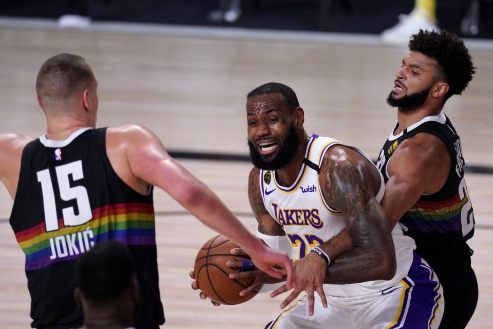 Lakers forward LeBron James tries to power his way to the basket between Nuggets guard Jamal Murray and center Nikola Jokic.