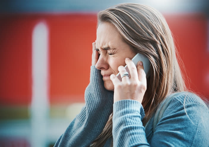 A young blonde woman grimaces, hand to her face as she hears something on her smart phone, obviously bad news.