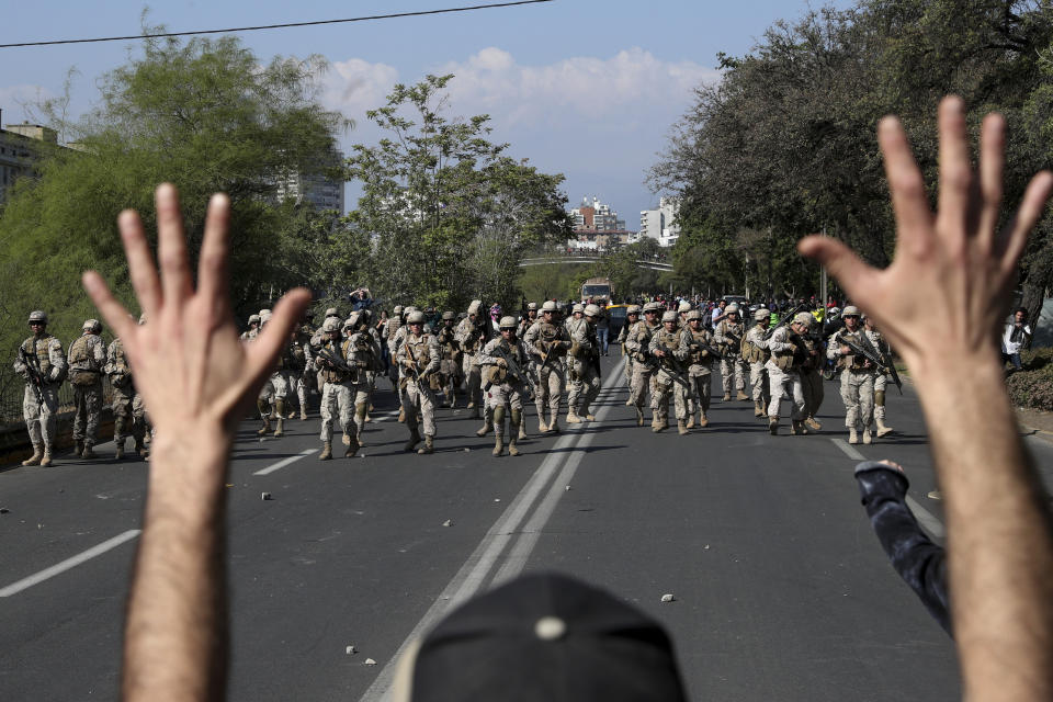 A demonstrator holds up his hands toward advancing soldiers during a protest as a state of emergency remains in effect in Santiago, Chile, Sunday, Oct. 20, 2019. Protests in the country have spilled over into a new day, even after President Sebastian Pinera cancelled the subway fare hike that prompted massive and violent demonstrations. (AP Photo/Esteban Felix)