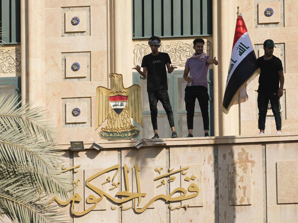 A supporter of Shiite cleric Muqtada al-Sadr waves a national flag from the roof of the Government Palace during a demonstration in Baghdad, Iraq, Monday, Aug. 29, 2022. Al-Sadr, a hugely influential Shiite cleric announced he will resign from Iraqi politics and his angry followers stormed the government palace in response. The chaos Monday sparked fears that violence could erupt in a country already beset by its worst political crisis in years. (AP Photo/Hadi Mizban)