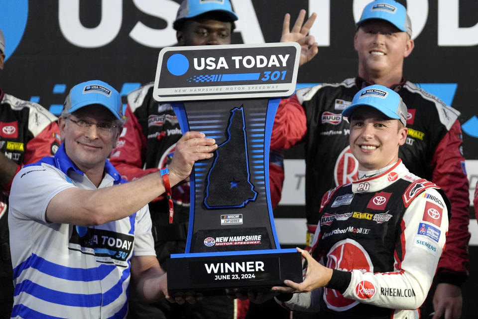 Howard Altschiller, left, executive editor of Seacoast Media Group, presents Christopher Bell, right, with the winner's trophy during ceremonies after Bell won the NASCAR Cup Series race, Sunday, June 23, 2024, at New Hampshire Motor Speedway in Loudon, N.H. (AP Photo/Steven Senne)