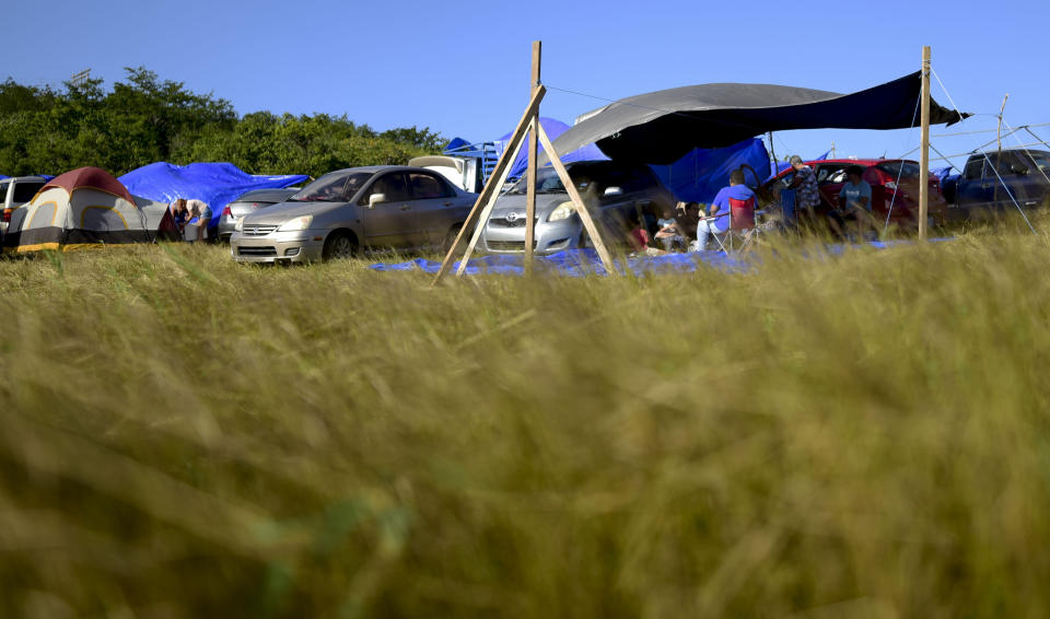 In this Friday, Jan. 10 photo, people shade themselves under a tarp on a private hay farm where residents from the Indios neighborhood affected by earthquakes set up shelter amid aftershocks in Guayanilla, Puerto Rico. A 6.4 magnitude quake that toppled or damaged hundreds of homes in southwestern Puerto Rico is raising concerns about where displaced families will live, while the island still struggles to rebuild from Hurricane Maria two years ago. (AP Photo/Carlos Giusti)