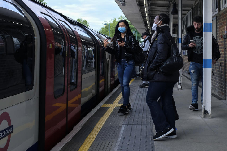 Commuters, some wearing protective masks to protect against coronavirus stand on the platform at Leytonstone underground station, in London, Monday, May 18, 2020. Britain's Prime Minister Boris Johnson announced last Sunday that people could return to work if they could not work from home. (AP Photo/Alberto Pezzali)