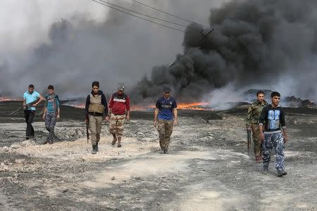 Tribal fighters walk as fire and smoke rises from oil wells, set ablaze by Islamic State militants before IS militants fled the oil-producing region of Qayyara, Iraq, November 1, 2016. REUTERS/Alaa Al-Marjani