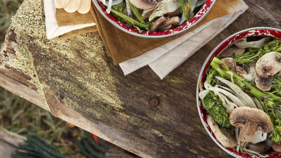 marinated mushroom and charred broccolini salads in bowls on a table outside