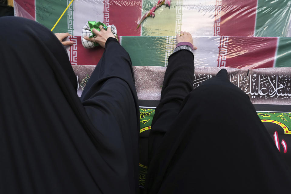 Mourners touch flag-draped coffins of unknown Iranian soldiers who were killed during the 1980-88 Iran-Iraq war, whose remains were recently recovered in the battlefields, during their funeral procession, in Tehran, Iran, Tuesday, Dec. 27, 2022. (AP Photo/Vahid Salemi)