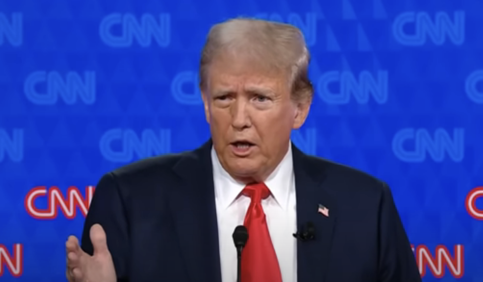 Donald Trump speaking at a CNN event, wearing a dark suit and red tie against a backdrop with CNN logos