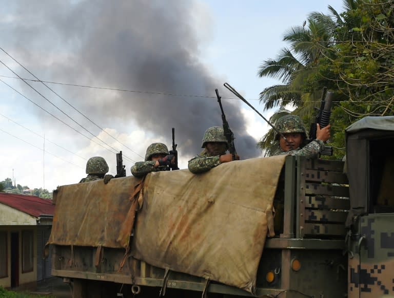 Philippine Marines aboard their truck drive past as smoke billows after military helicopters fired rockets at militant positions in Marawi on the southern island of Mindanao