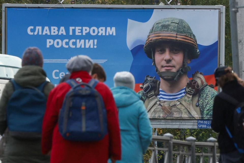 People gather at a tram stop in front of a board displaying a portrait of Russian service member Sergei Tserkovniy in Saint Petersburg, Russia September 21, 2022. A slogan on the board reads: 