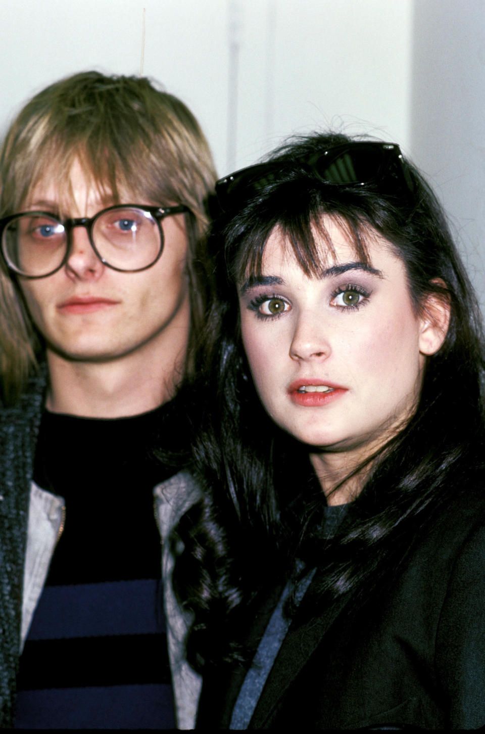 Two individuals posing for a photo, one with glasses and a striped top, the other with sunglasses atop their head