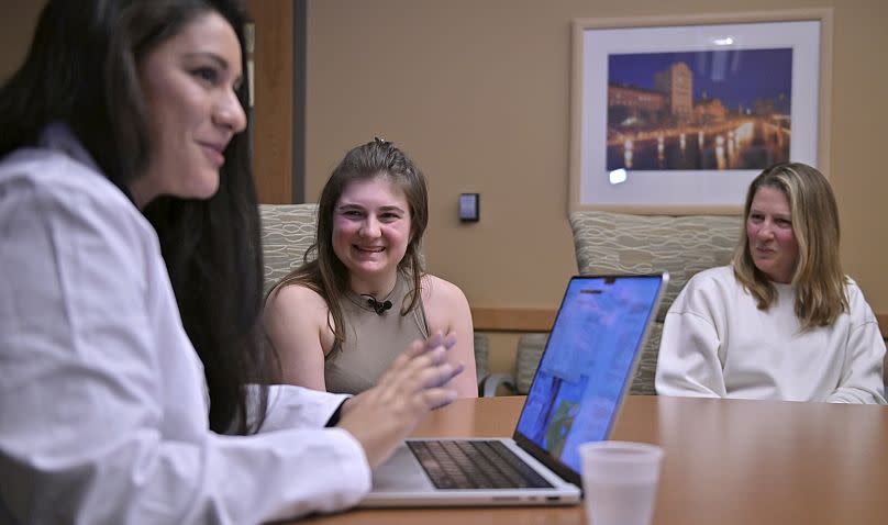 Alexis Bogan (center) and her mother Pamela Bogan (right) react to hearing a recreation of her lost voice via a prompt typed by Dr. Fatima Mirza (left).