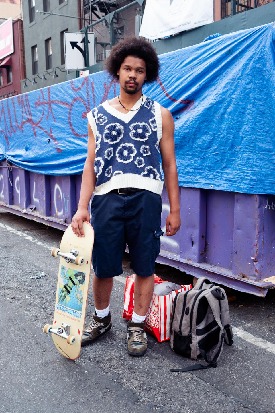 man wearing a sweater vest holding a skateboard in new york