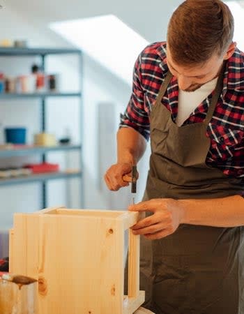 A person in a brown apron uses a tool to fix a furnishing.