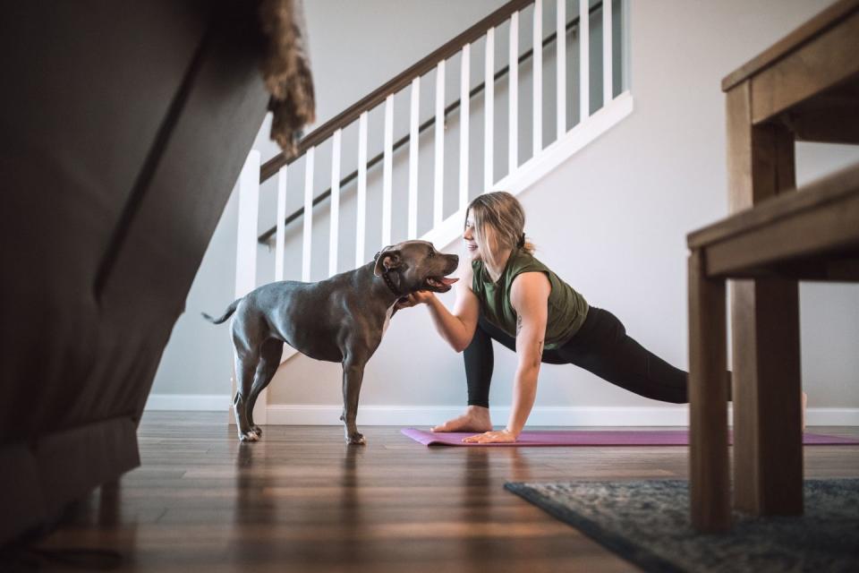 woman at home doing lunges on yoga matt while stroking dog