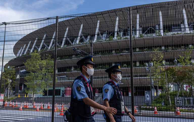 ficiales de policía con máscaras patrullan junto al Estadio Olímpico de Tokio el 21 de julio de 2021 en Tokio, Japón. A tan solo dos días de la ceremonia de apertura de los Juegos Olímpicos, Toshiro Muto, el jefe del comité organizador de Tokio 2020 ha declarado que no descartará la cancelación de los Juegos ya que más de setenta personas asociadas al evento ya han dado positivo por coronavirus.