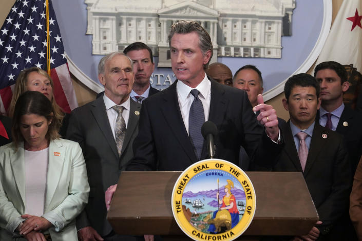 California Gov. Gavin Newsom, with a group of lawmakers behind him, speaks at a lectern.