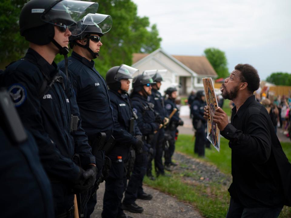 A demonstrator holding a sign jumps up and down so police officers behind the front lines could see it, outside the Oakdale, Minn,, home of fired Minneapolis police Officer Derek Chauvin on Wednesday evening, May 27, 2020. The mayor of Minneapolis called Wednesday for criminal charges against the white police officer seen on video kneeling against the neck of Floyd George, a handcuffed black man who complained that he could not breathe and died in police custody. (Jeff Wheeler/Star Tribune via AP)