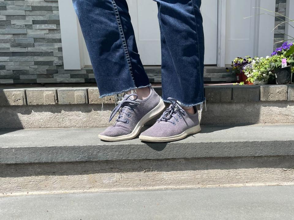 a model wearing a pair of purple all birds tree runner shoes with jeans, good housekeeping's pick for best travel walking shoes for women