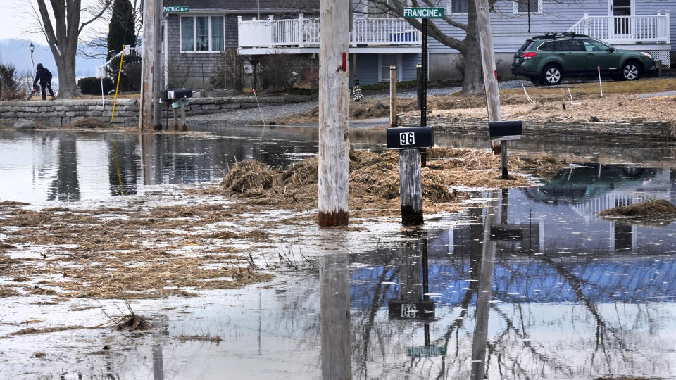 While her road and neighbor's mailboxes are covered by high tide waters, Diane Levesque, left, uses a leaf blower to clear marsh grass from her yard, which was deposited during January 2024 storms, Friday, Feb. 9, 2024, in Hampton, N.H. Scientists say the back-to-back storms that lashed the Northeast in January were more of a sign of things to come than an anomaly. Many scientists who study the intersection of climate change, flooding, winter storms and sea level say such storms will arrive with increased frequency and ferocity. (AP Photo/Charles Krupa)