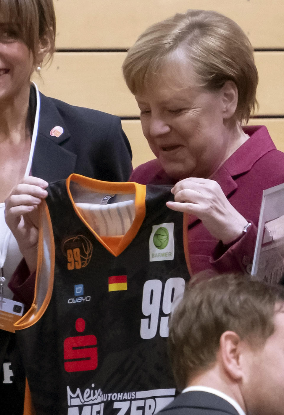 German Chancellor Angela Merkel holds a shirt as she visits the NINERS German first divisioner basketball youth teams (under 16 years and under 19 years) during her one-day visit in Chemnitz, eastern Germany, Friday, Nov. 16, 2018. Chemnitz has seen a few federal politicians show their faces since a 35-year-old local man was stabbed to death in August, allegedly by migrants, followed by a surge of violent right-wing protests. (AP Photo/Jens Meyer)