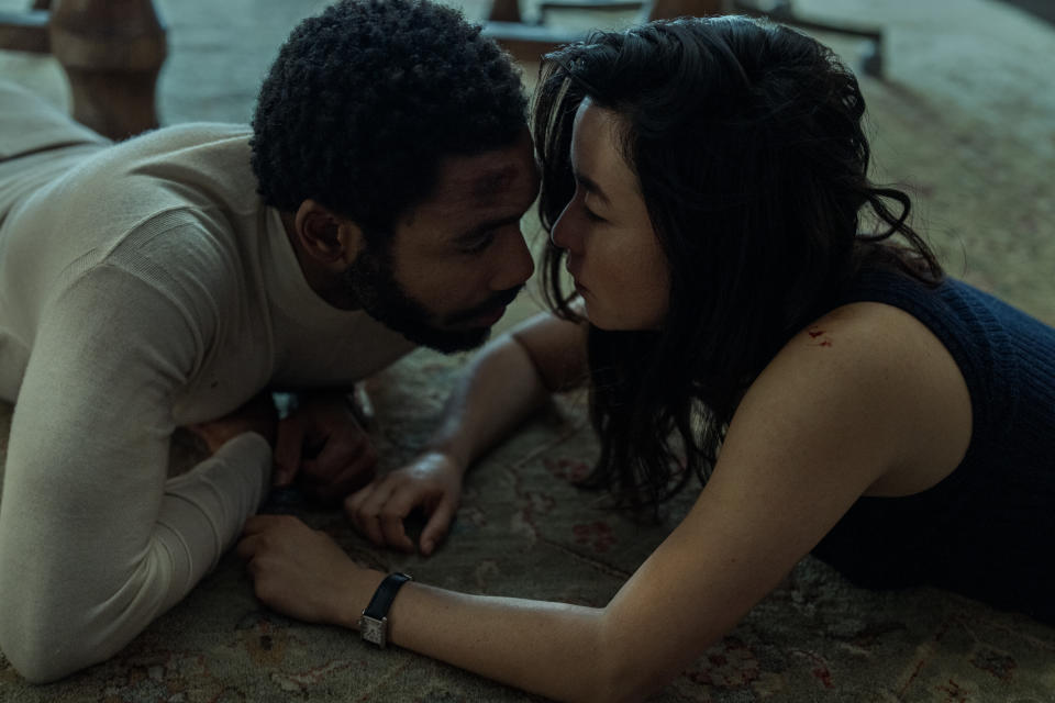 Donald Glover e Maya Erskine estão deitados no chão, quase se beijando.