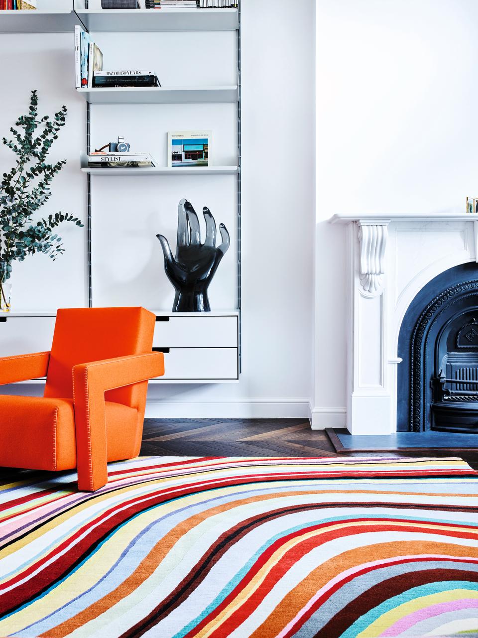 A living room with bright white walls, an orange armchair and multicolored rug