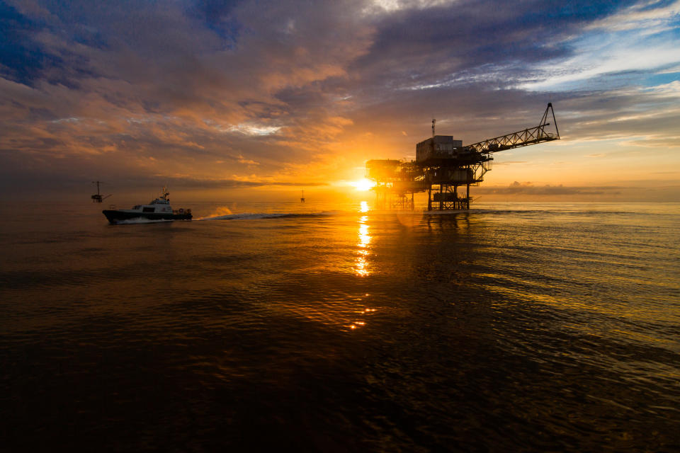 A ship near an offshore drilling rig at sunset.