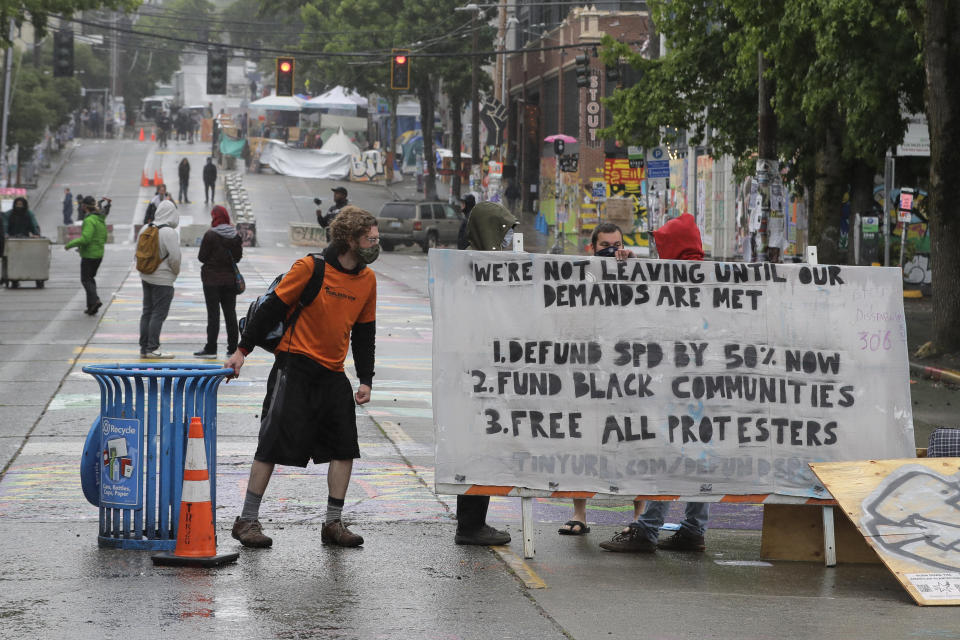 A protester moves a recycling container next to a sign listing demands after Seattle Department of Transportation workers removed concrete barricades at the intersection of 10th Ave. and Pine St., Tuesday, June 30, 2020 at the CHOP (Capitol Hill Occupied Protest) zone in Seattle. The area has been occupied by protesters since Seattle Police pulled back from their East Precinct building following violent clashes with demonstrators earlier in the month. (AP Photo/Ted S. Warren)