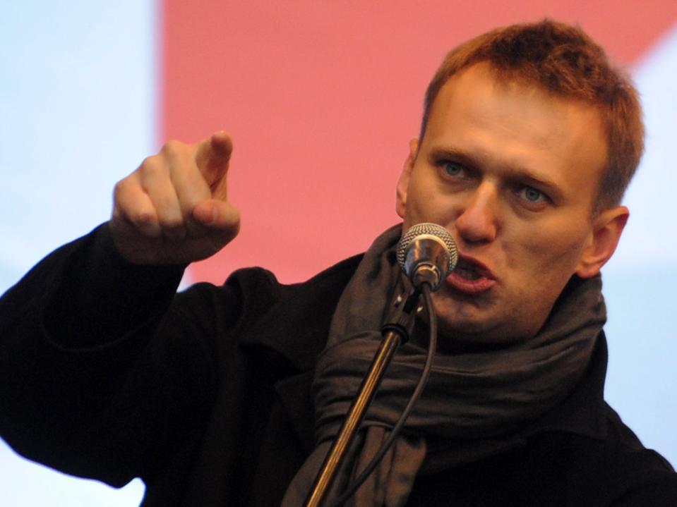 Alexei Navalny speaks into a microphone and points into the distance.