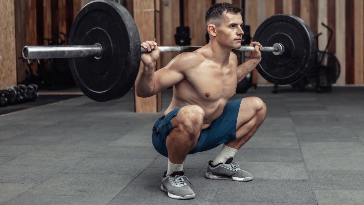  Man at the bottom of a barbell back squat during gym workout. 