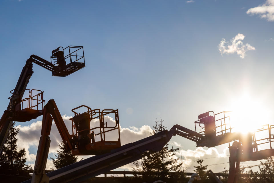 Five cherry pickers with a partly cloudy sky in the background