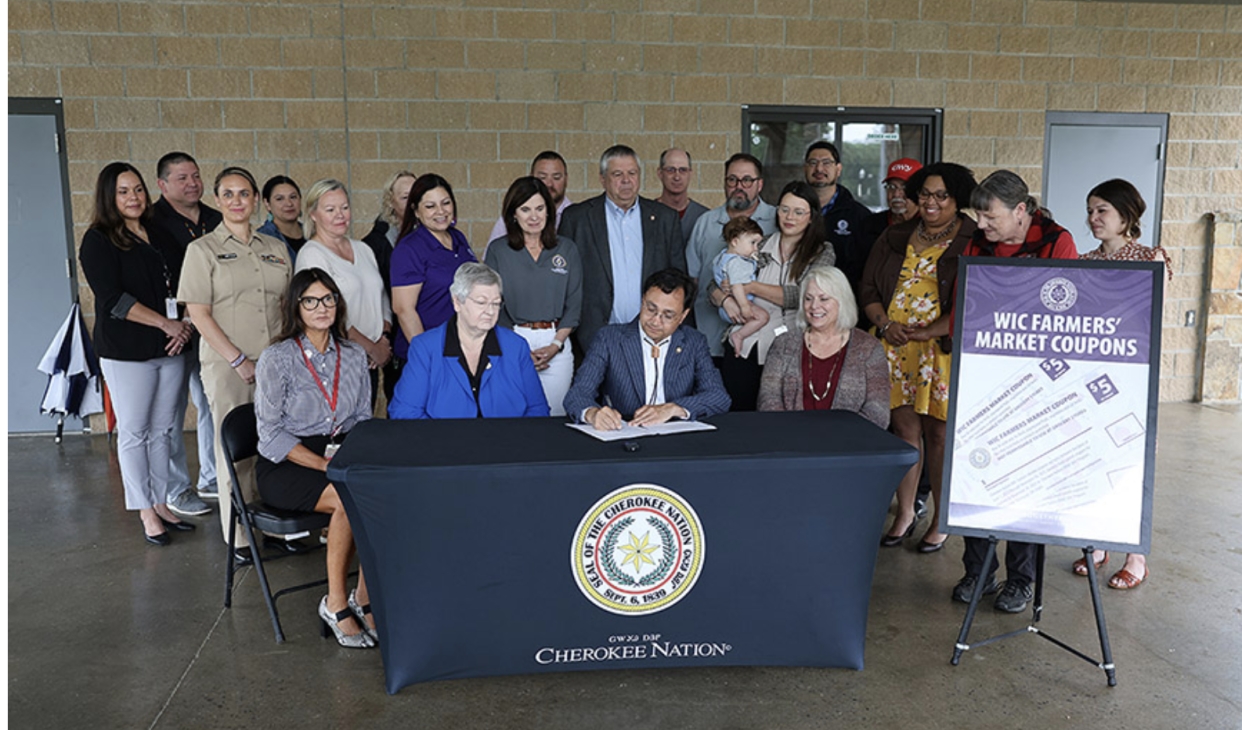 (L-R): Seated: Senior Director of Public Health Lisa Pivec, Secretary of State Tina Glory Jordan, Cherokee Nation Principal Chief Chuck Hoskin Jr., Executive Director of Commerce Anna Knight are surrounded by Cherokee Nation Public Health employees, cabinet officials, WIC participants and Tahlequah Farmer’s Market representatives during a WIC announcement Friday in Tahlequah. (Photo/Cherokee Nation)