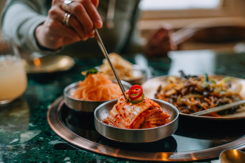 Woman enjoying traditional Korean fermented vegetables (Banchan) with chopsticks. Korean food and cultures.