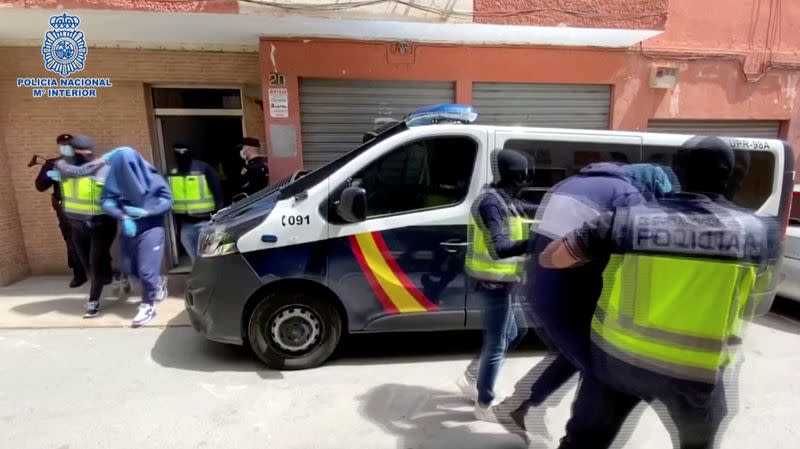 Men with heads covered with towels are led out of a building to the cars, in Almeria