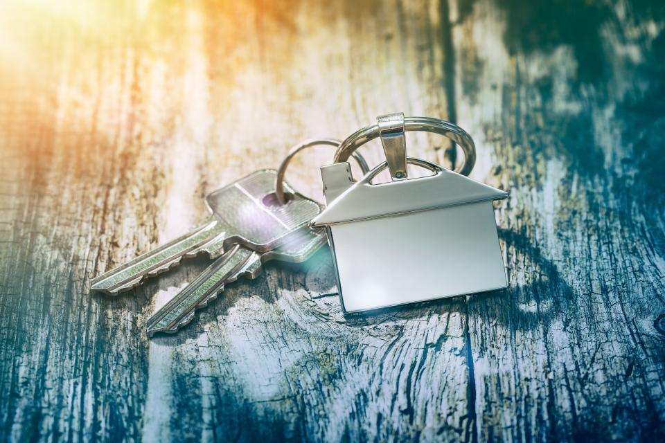 House key on a house shaped keychain on wooden table. Photo: Getty