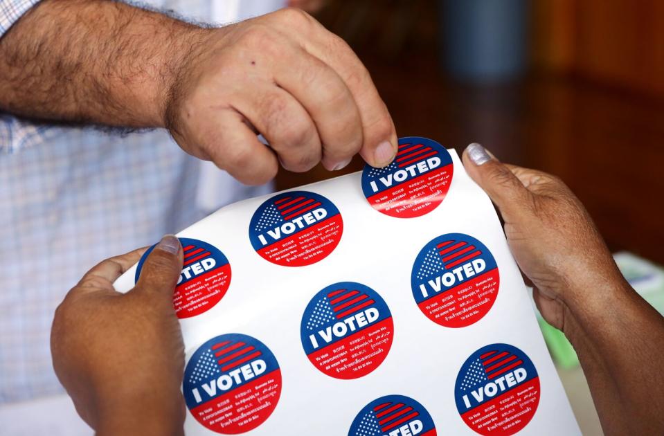 A man peels an "I voted" sticker off a sheet held up by a poll worker