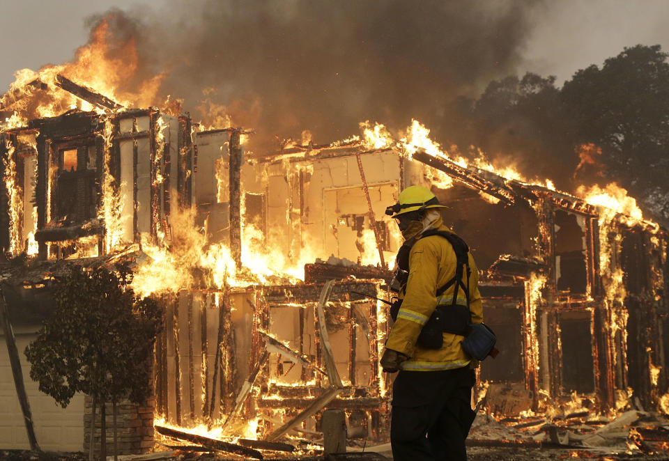 FILE - In this Oct. 9, 2017, file photo, a firefighter monitors a house burning in Santa Rosa, Calif. California power regulators slapped Pacific Gas and Electric with a $2.1 billion fine for igniting a series of deadly wildfires that landed the beleaguered utility in bankruptcy. The record penalty imposed Thursday, Feb. 27, 2020, in a an administrative law judge's decision boosts the punishment that had been agreed upon in a $1.7 billion settlement announced in December. The increased punishment includes a $200 million payment earmarked for the people who lost family and property in catastrophic wildfires caused by PG&E's outdated electrical grid and negligence during 2017 and 2018. (AP Photo/Jeff Chiu, File)