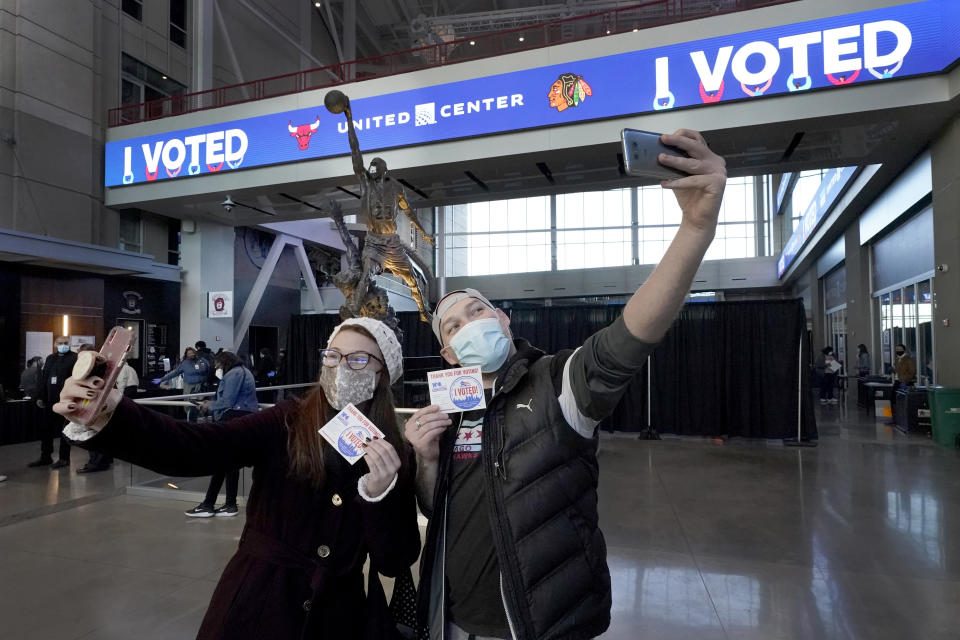 Samantha Jones, left, and Peter Vina take selfies near the Michael Jordan statue on Election Day, Tuesday, Nov. 3, 2020, in the atrium of the United Center, transformed into a super voting site in Chicago. (AP Photo/Charles Rex Arbogast)