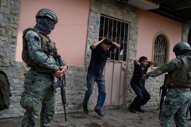 Dos soldados obligan a dos hombres a ejercitarse como castigo por no traer las licencias adecuadas para sus motocicletas, el sábado 30 de septiembre de 2023, en Durán, ciudad hermana de Guayaquil, Ecuador. (AP Foto/Rodrigo Abd)