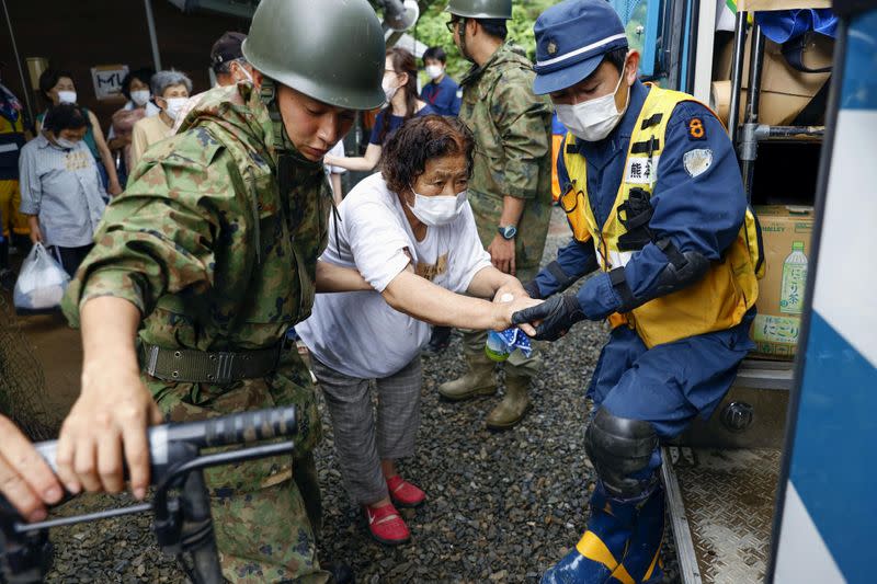 An evacuee is helped by rescue workers as she moves from a shelter to another shelter in Kuma town