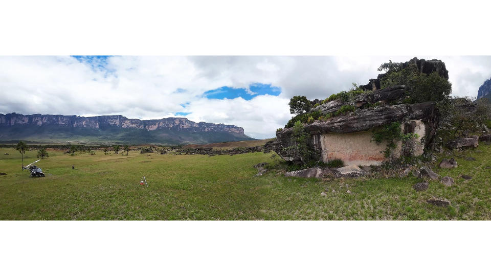 A panoramic photo of a grassy plain with a landed helicopter on it