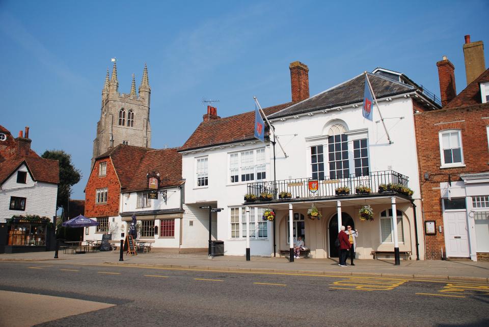 Tenterden, England - April 17, 2019: People stand by the historic Town Hall at Tenterden in Kent. The building dates from 1790. The Woolpack pub and hotel stands next door.