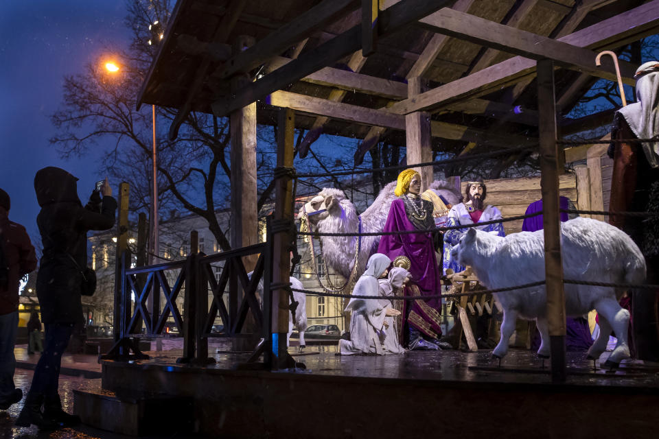 A woman photographs the Nativity scene installed for upcoming Christmas celebrations in Cathedral Square in Vilnius, Lithuania, Saturday, Dec. 23, 2023. (AP Photo/Mindaugas Kulbis)