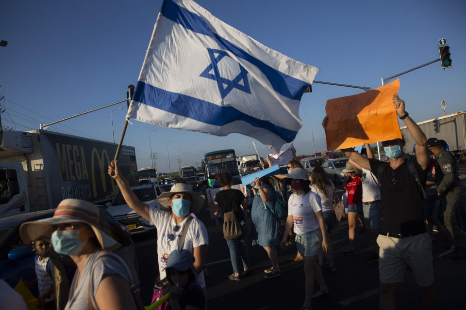 Israeli social workers wave a national flag as they block a main road during a protest against the economic situation in the central Israeli town of Kfar Ahim, Thursday, July 9, 2020. With a new outbreak of coronavirus devastating Israel's economy, one of Prime Minister Benjamin Netanyahu's closest confidants was dispatched on to a TV studio on a recent day to calm the nerves of a jittery nation. Instead, he dismissed the public's economic pain as "BS." (AP Photo/Sebastian Scheiner)