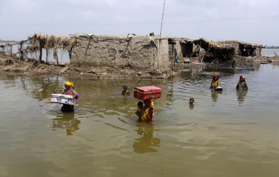 Women carry belongings salvaged from their flooded home after monsoon rains, in the Qambar Shahdadkot district of Sindh Province, of Pakistan, Tuesday, Sept. 6, 2022. More than 1,300 people have been killed and millions have lost their homes in flooding caused by unusually heavy monsoon rains in Pakistan this year that many experts have blamed on climate change. (AP Photo/Fareed Khan)