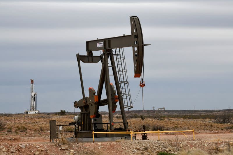 FILE PHOTO: A pump jack operates in front of a drilling rig owned by Exxon near Carlsbad