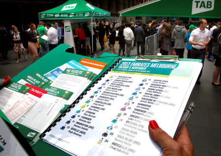 An official holds a list of the Melbourne Cup horses and jockeys as people place bets at an outdoor betting tent organised by Australian gambling company Tabcorp Holdings Ltd (TAB) in central Sydney, Australia, November 5, 2013. REUTERS/David Gray/File photo