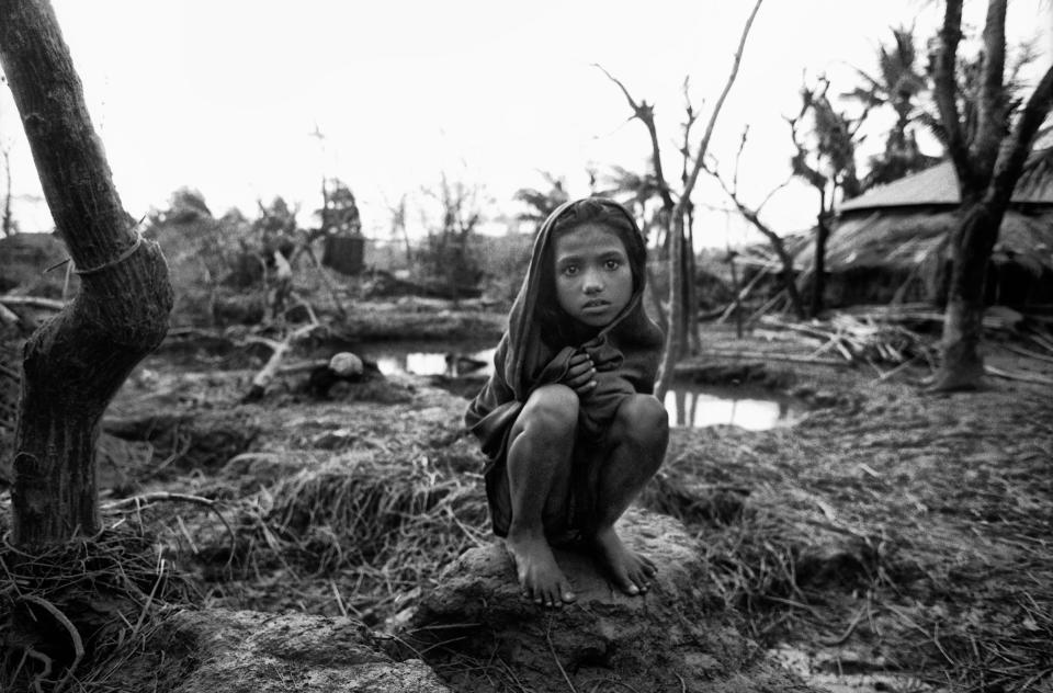 A girl crouches near the remains of her home in the aftermath of a deadly storm in Anwara, Chittagong, Bangladesh, 1991.