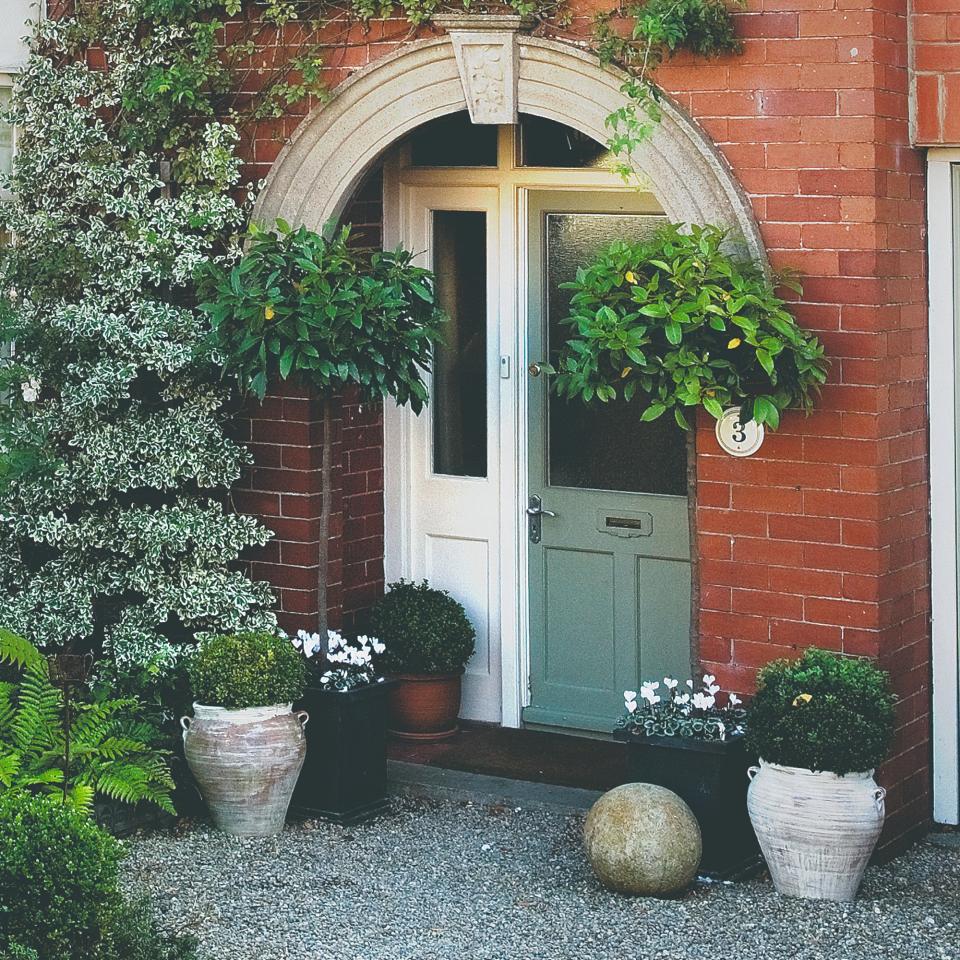 A red-brick house with a potted bay tree by its front door