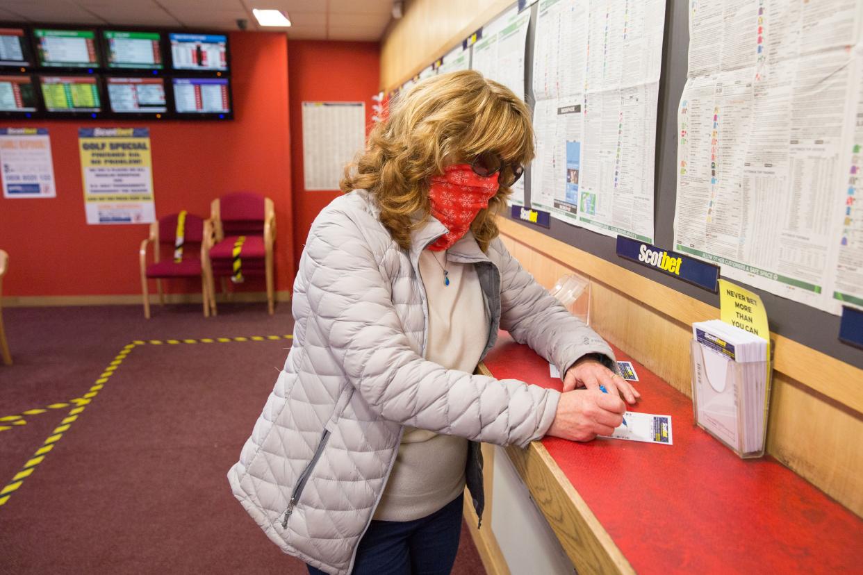 A woman wearing a face covering puts a bet on at the Scotbet Independent bookmakers shop, as coronavirus measures are relaxed to allow televisions and seating inside betting shops on July 22, 2020 in Chapelhall, Scotland.